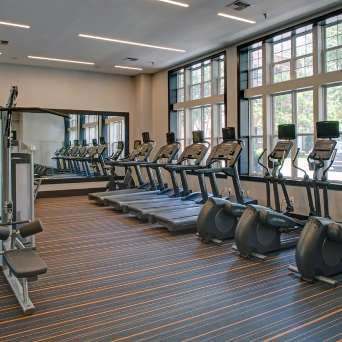 Spacious apartment fitness center featuring treadmills, elliptical machines, weight equipment, and large bright windows