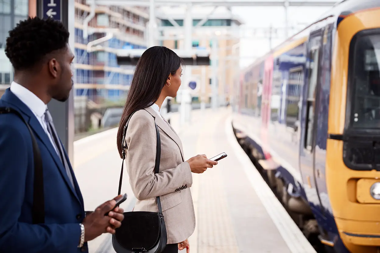 Professional commuters waiting on train station platform, holding smartphones, anticipating arriving commuter train