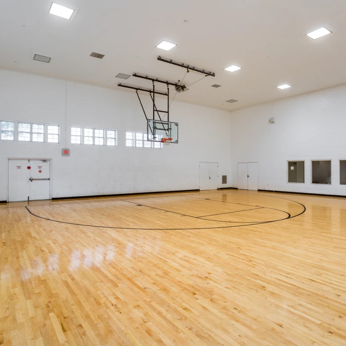 Spacious indoor basketball court featuring polished wood flooring and adjustable ceiling-mounted basketball hoop