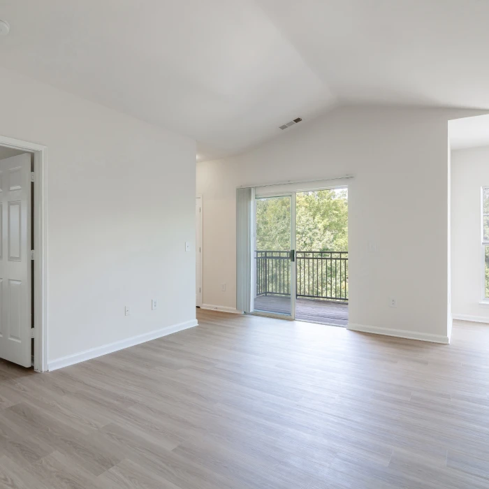 Bright empty apartment living area featuring light wood flooring, white walls, and private balcony access