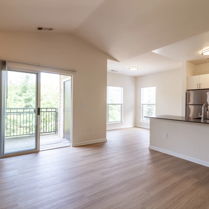 Open-concept living space in empty apartment with sliding glass door leading to outdoor balcony area