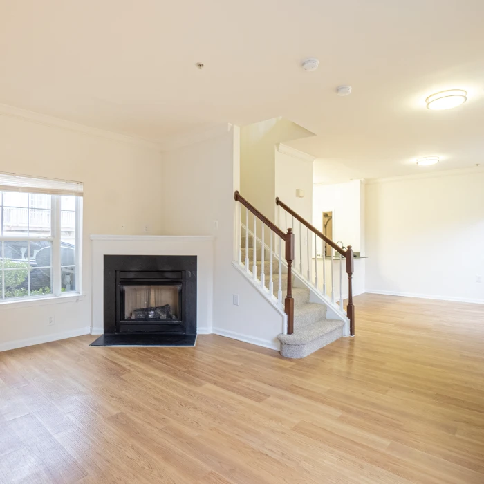 Spacious apartment living room featuring light wood flooring, cozy fireplace, and carpeted staircase access
