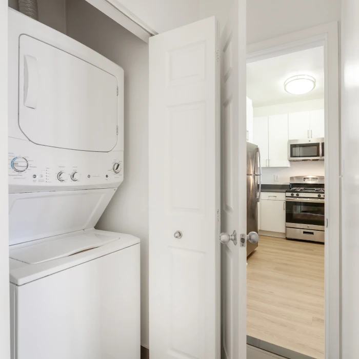 In-unit stacked washer and dryer set located beside a modern apartment kitchen entrance view