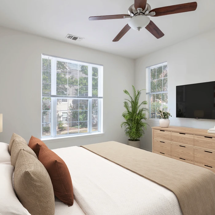 Modern furnished bedroom featuring warm neutral tones, large windows, flat-screen television, and indoor greenery decor