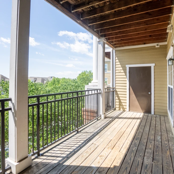 Covered apartment balcony space offering privacy, wooden flooring, and elevated view of surrounding treetops