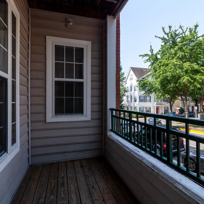 Apartment balcony with wooden floor, green railing, and view of residential neighborhood with trees and cars
